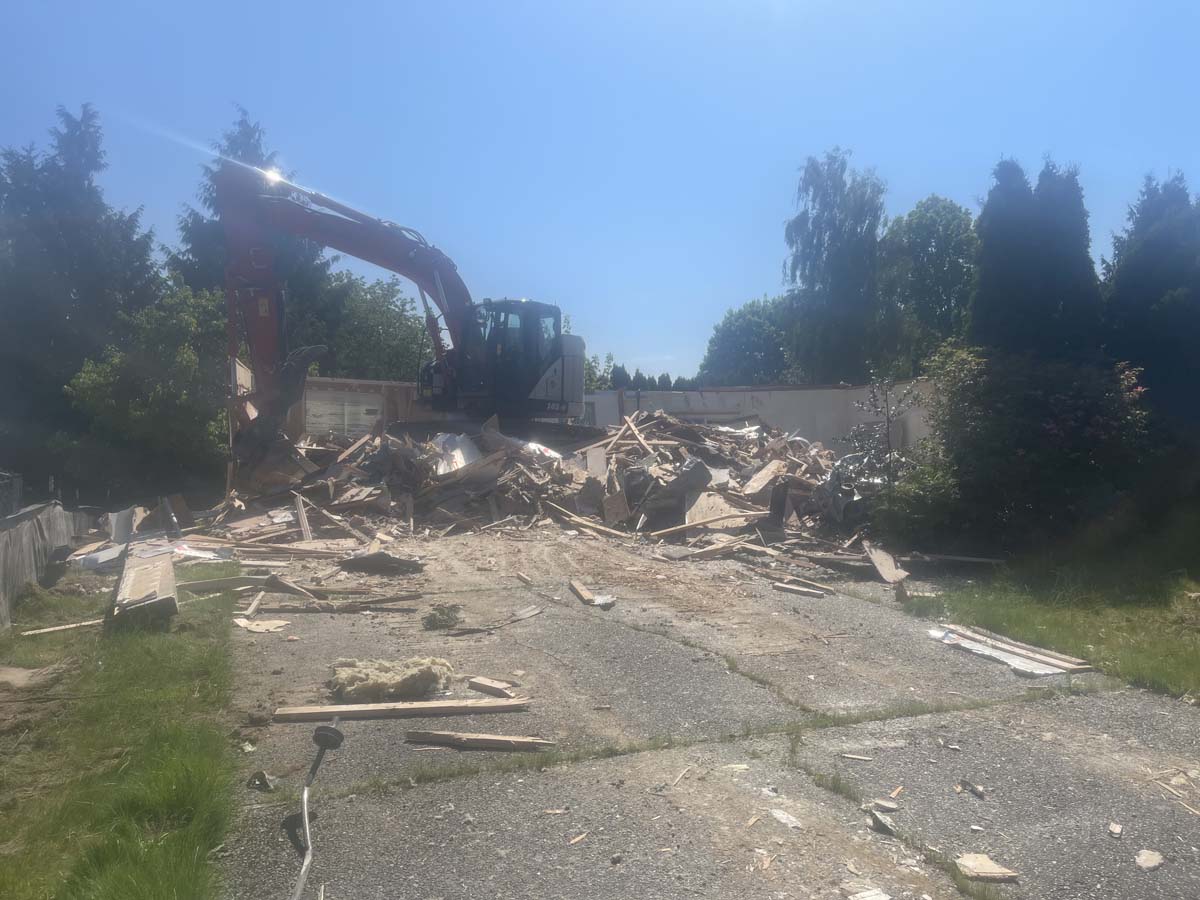 An excavator mid-demolition tearing into a structure, rubble scattered across the site
